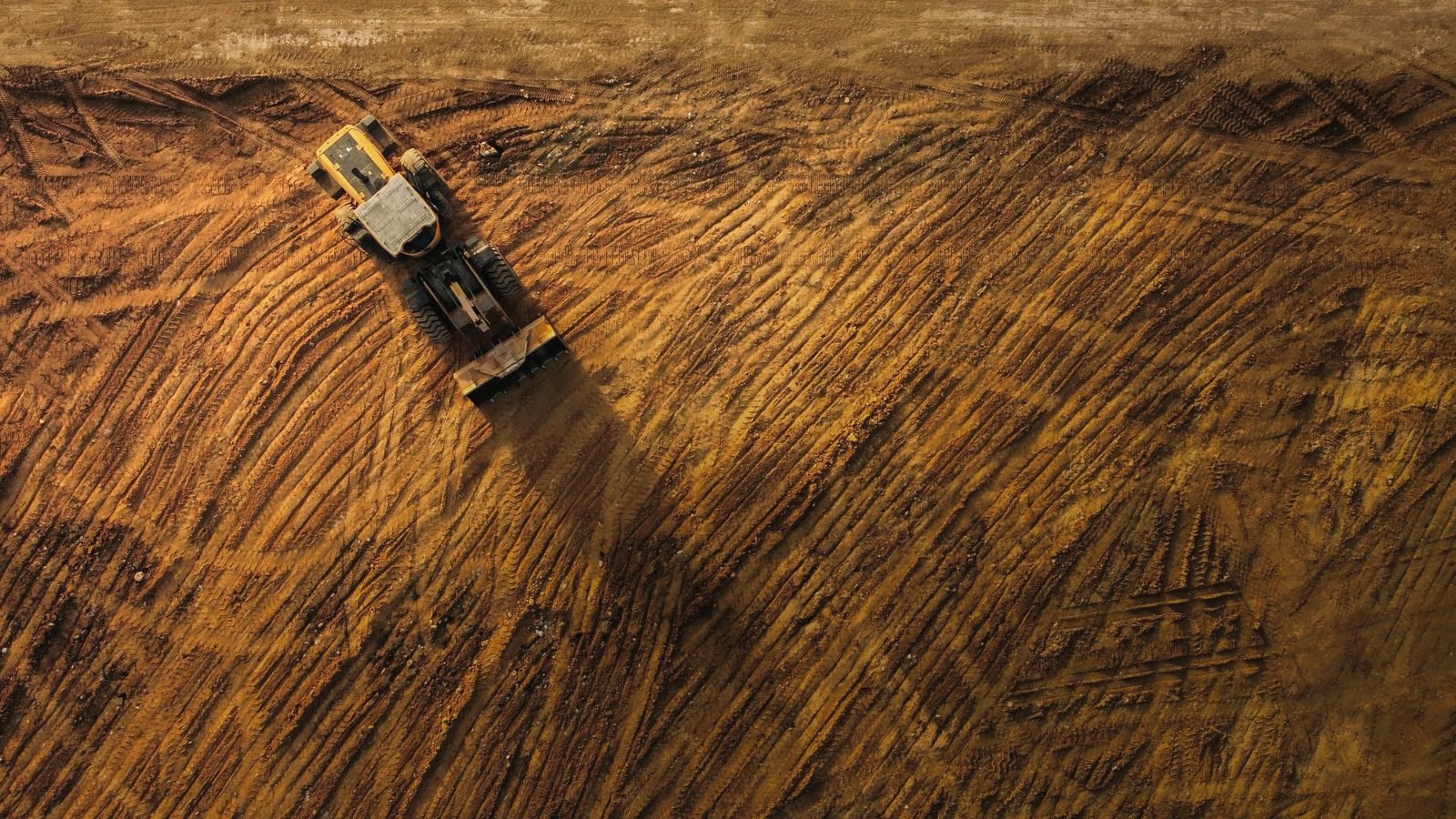 Overhead view of a bulldozer leaving track lines across graded dirt