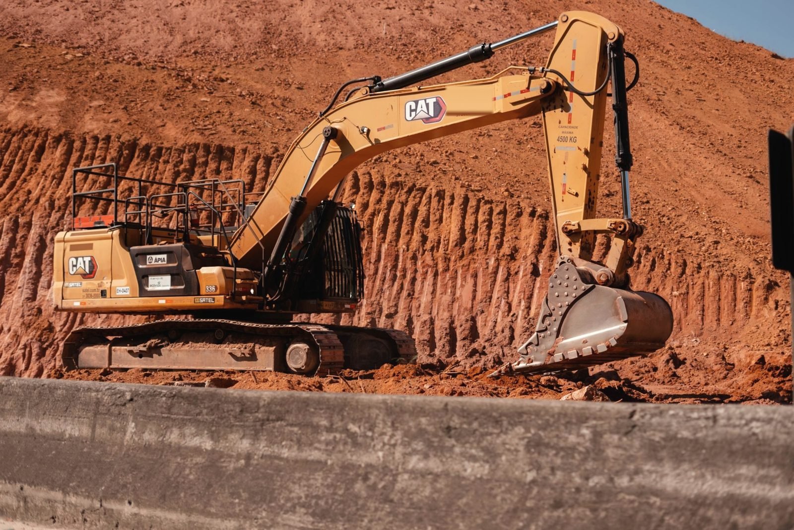 Tracked excavator cutting into a bank of red clay